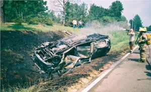 car on fire in ditch, flipped upside down while firefighters try to extinguish it